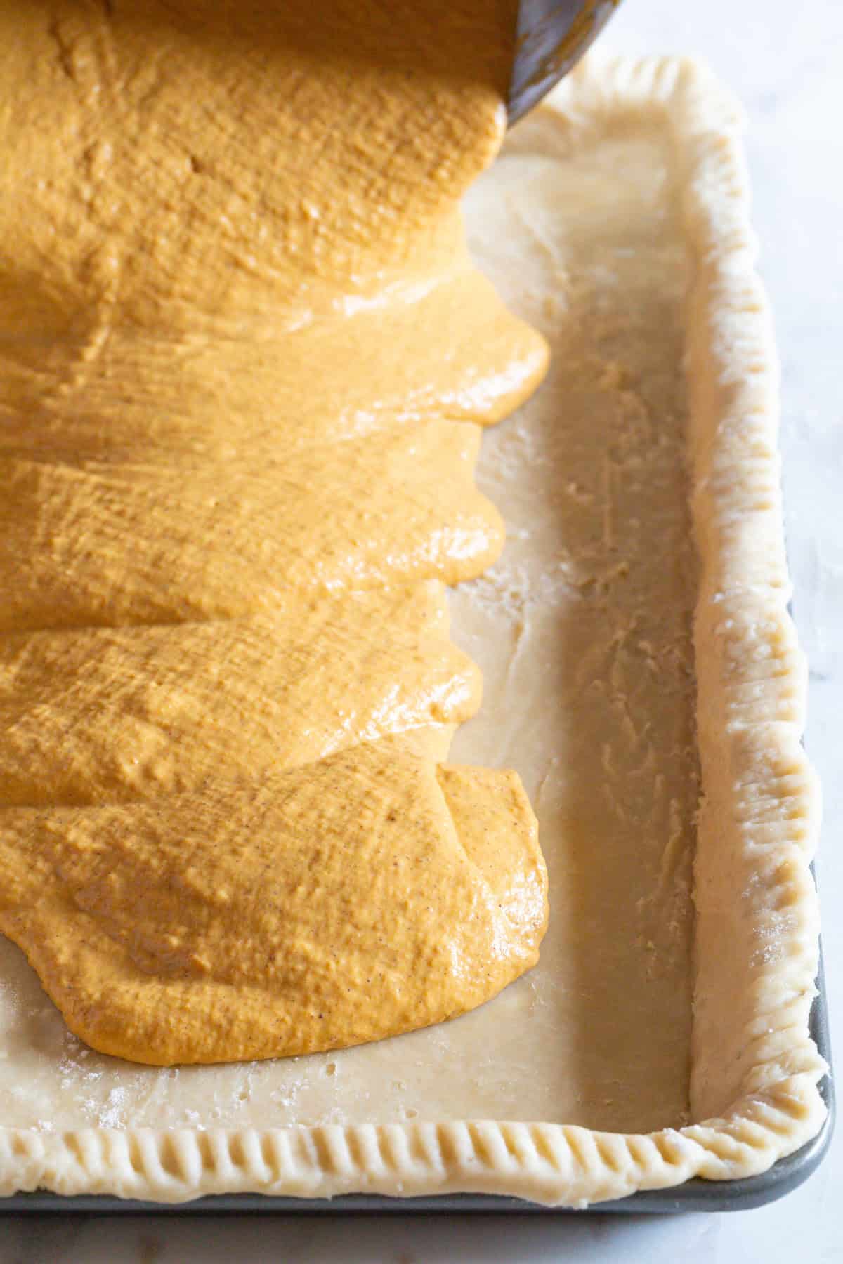 pouring pumpkin filling into pie crust