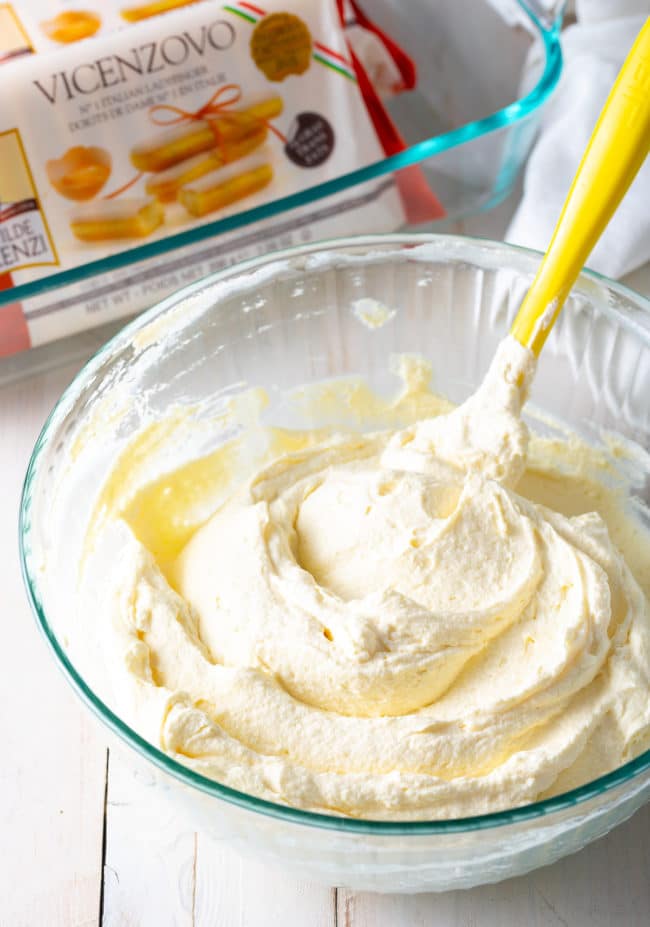 Spatula combining the mascarpone and heavy cream in a glass bowl.