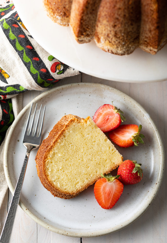 Single slice of cream cheese pound cake on a plate with some strawberries next to it 
