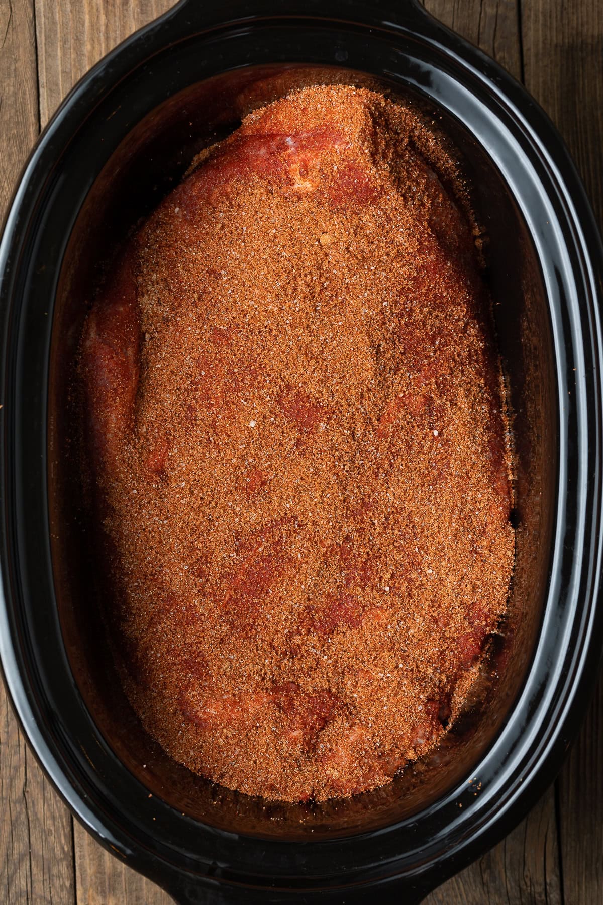 Uncooked brisket covered in spices in a slow cooker.