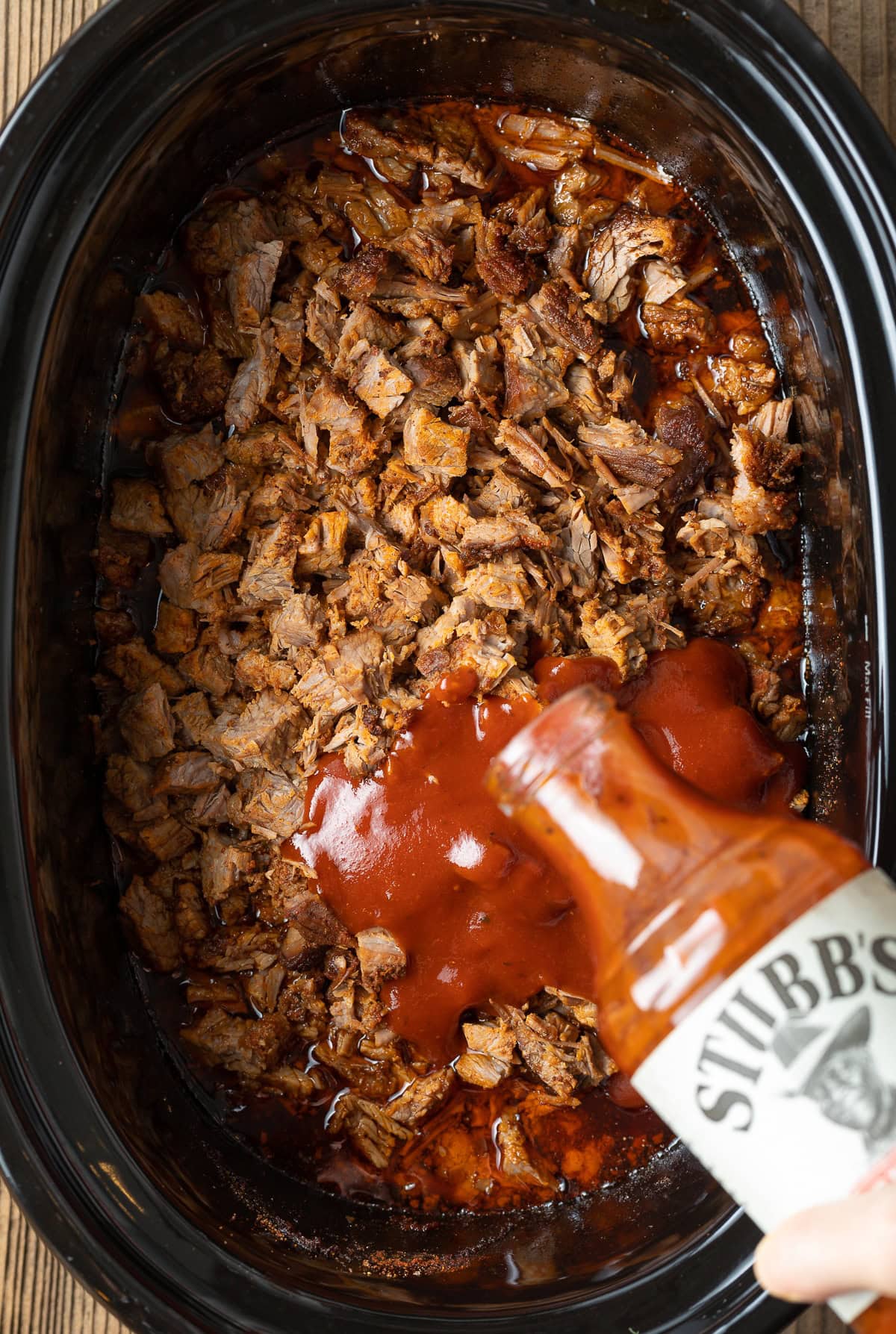 Adding bbq sauce to chopped beef in a slow cooker.