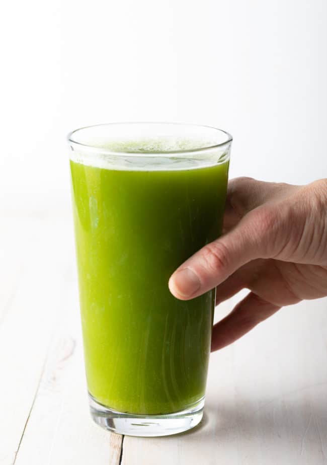 Hand holding a glass of celery juice.