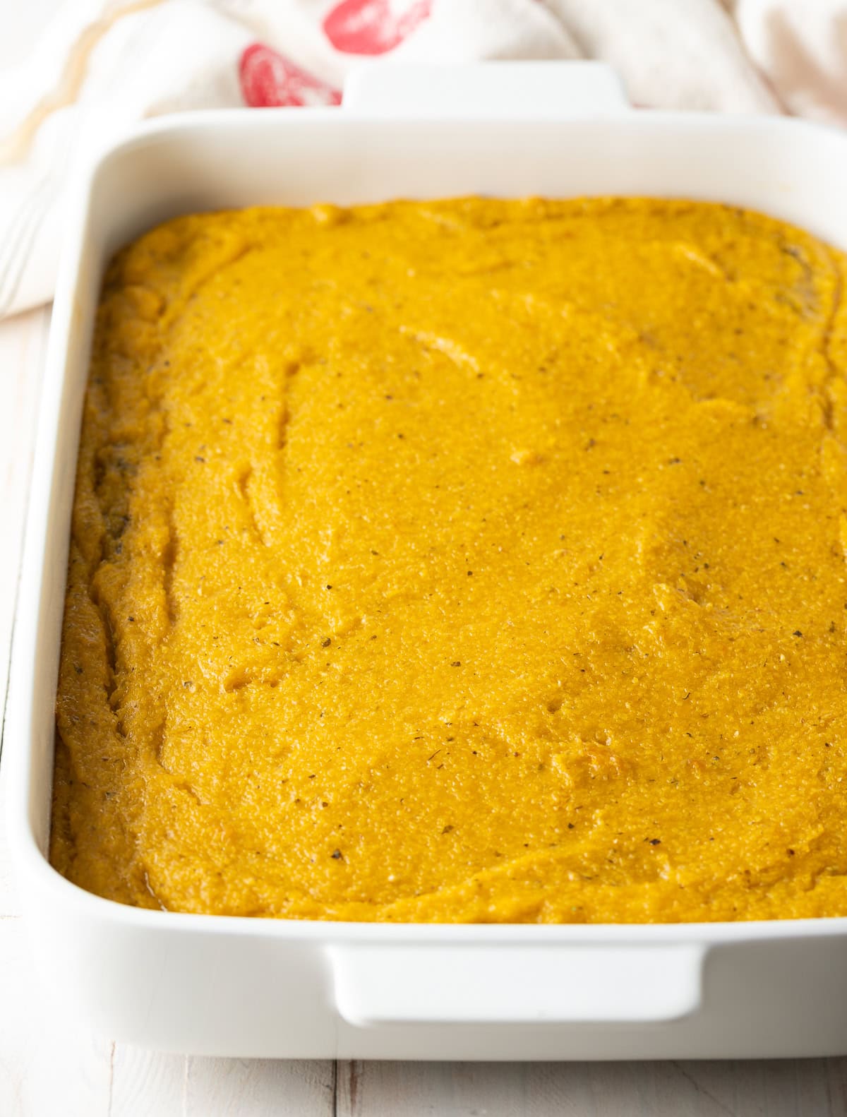 Thick layer of polenta poured into a baking dish.