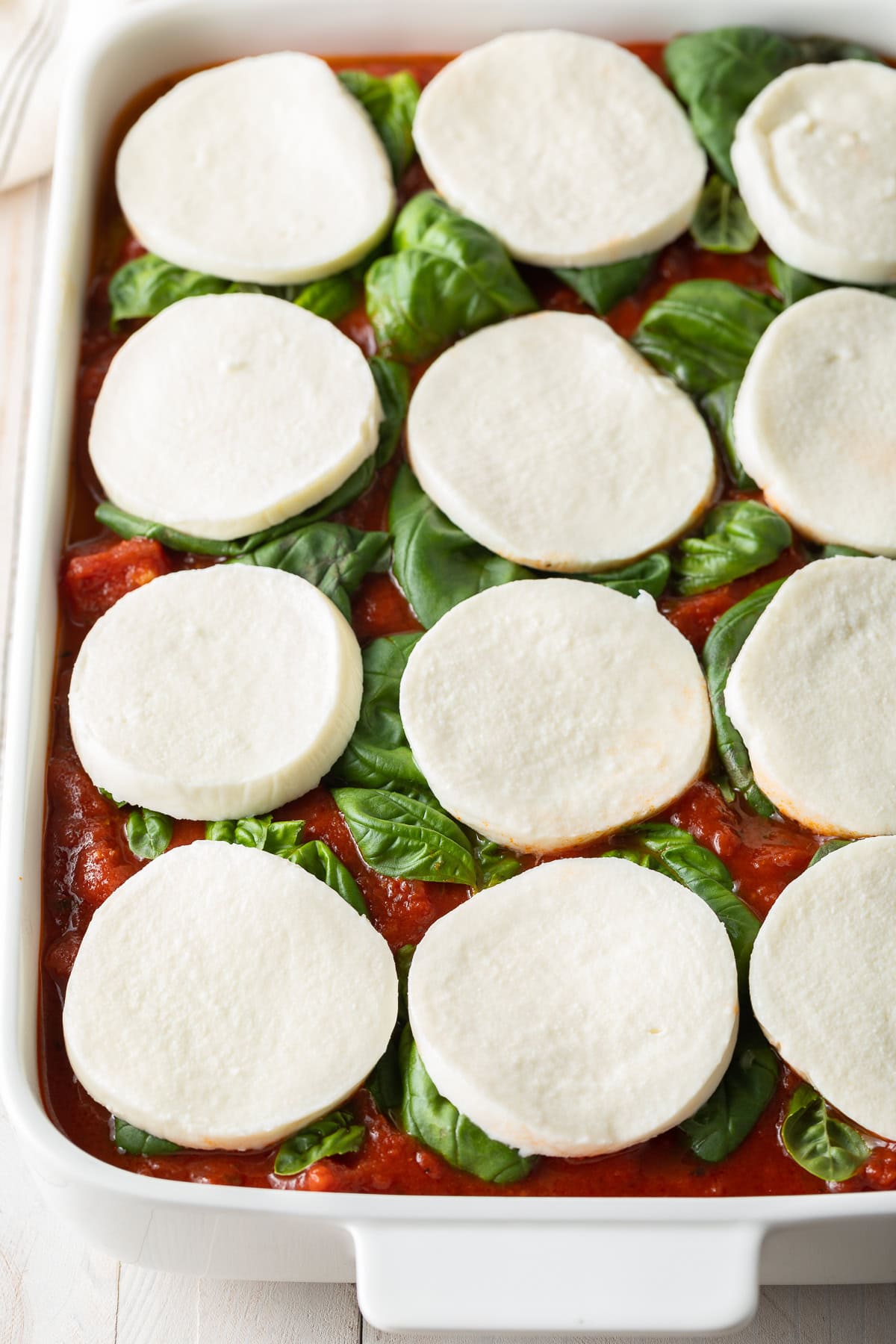 Top down view of baking dish filled with baked polenta and uncooked sauce, basil and mozzarella.