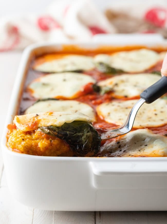 Lifting a square of polenta out of a baking dish.