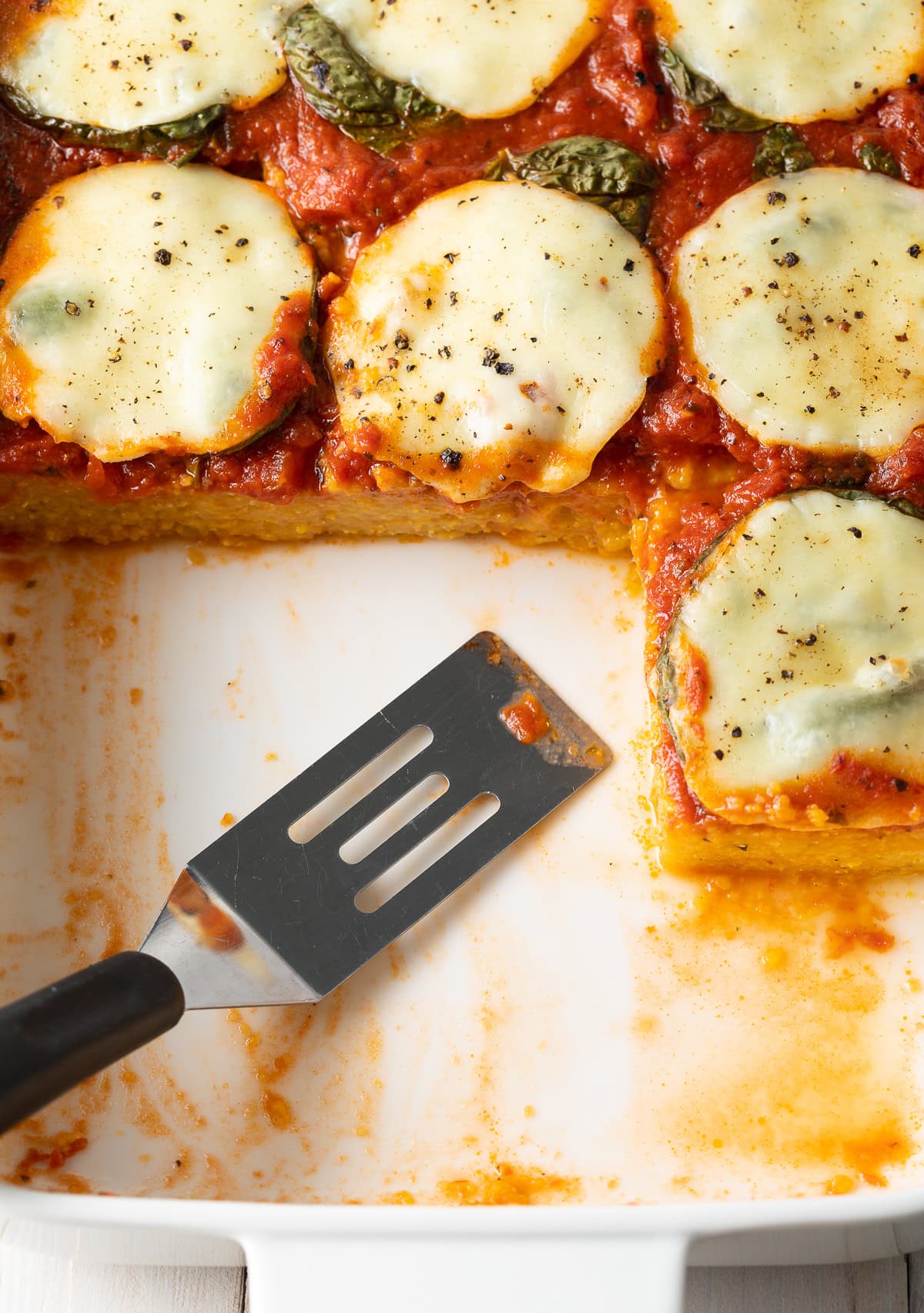 Top down view of baking dish with baked polenta and a slice removed.