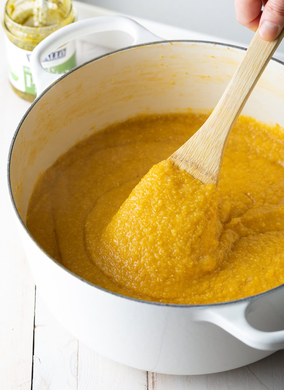 Cooked polenta in a pot being stirred by a wooden spoon.