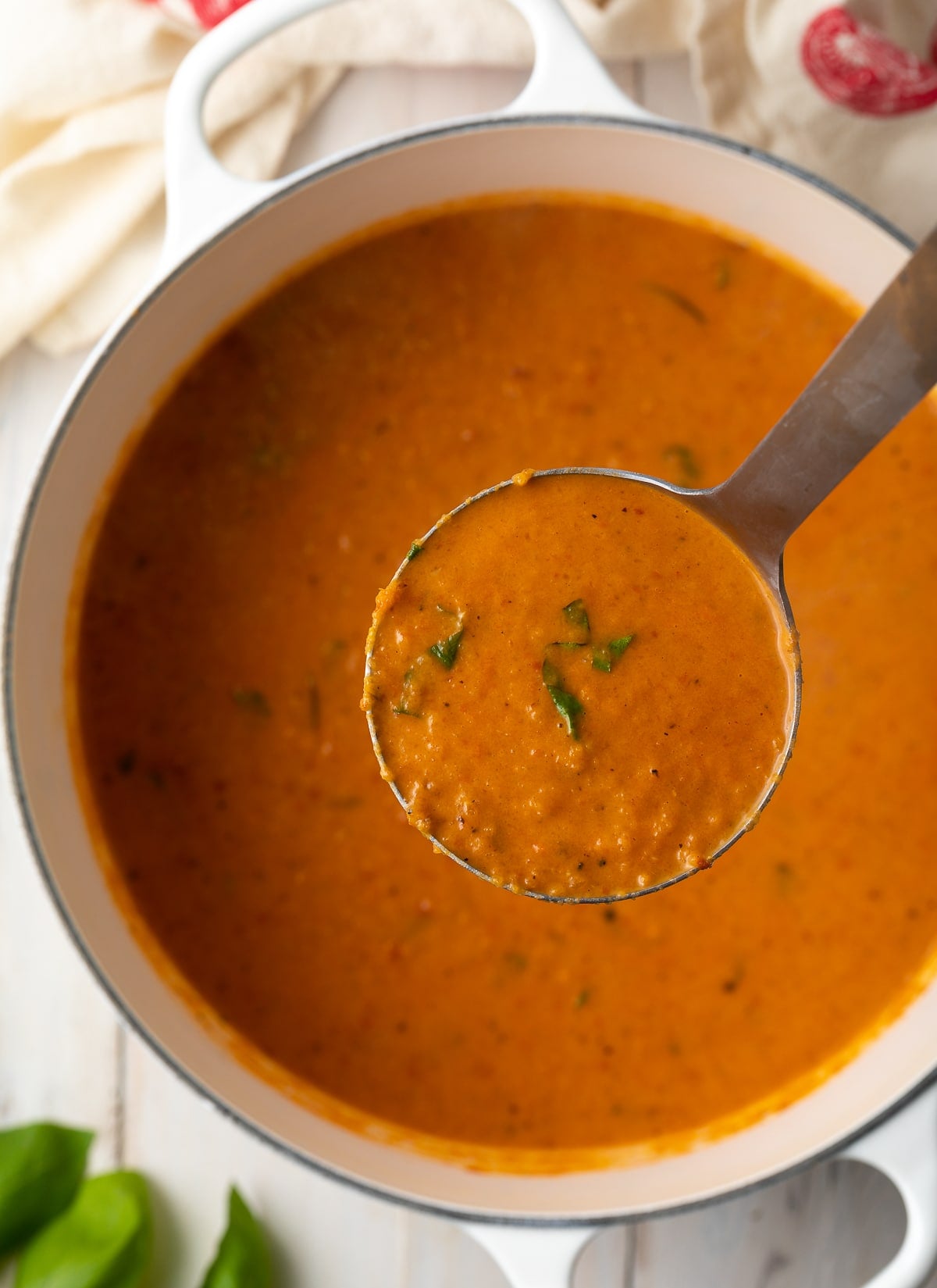 Ladle of creamy tomato soup being held above the pot of soup. 