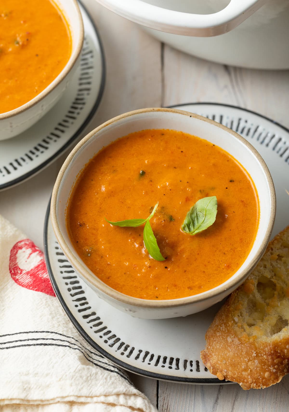 Roasted tomato soup in a bowl with basil sprigs on top and a piece of bread on the side. 