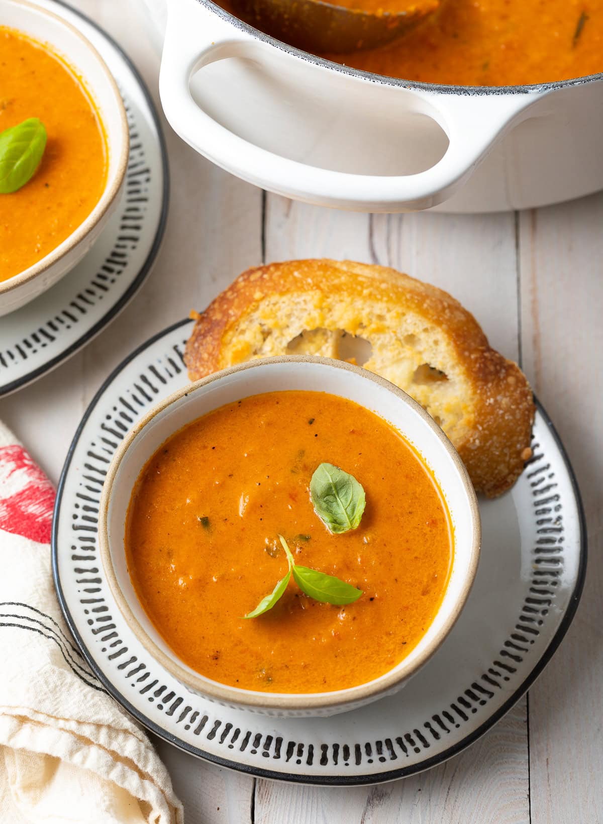 Two bowls of roasted tomato soup with a pot of more soup in the background. 