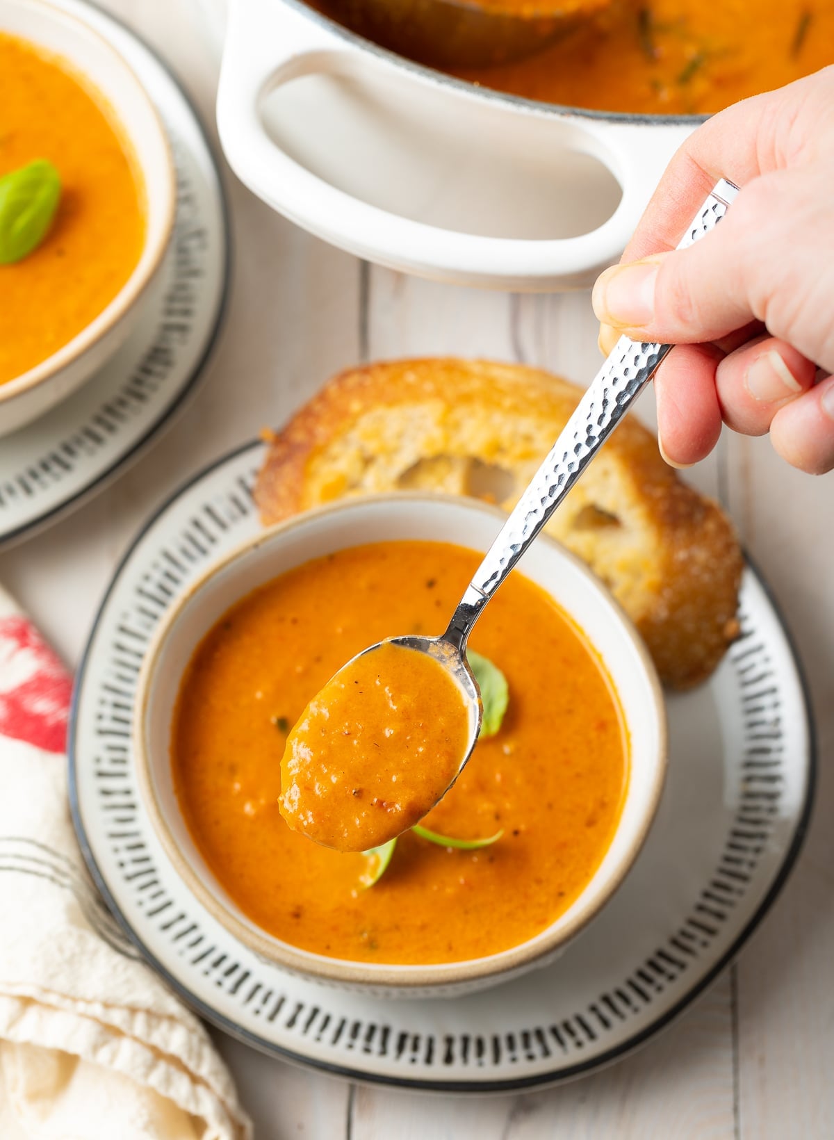 Bowl of tomato soup with a hand holding a spoonful of soup above the bowl. 