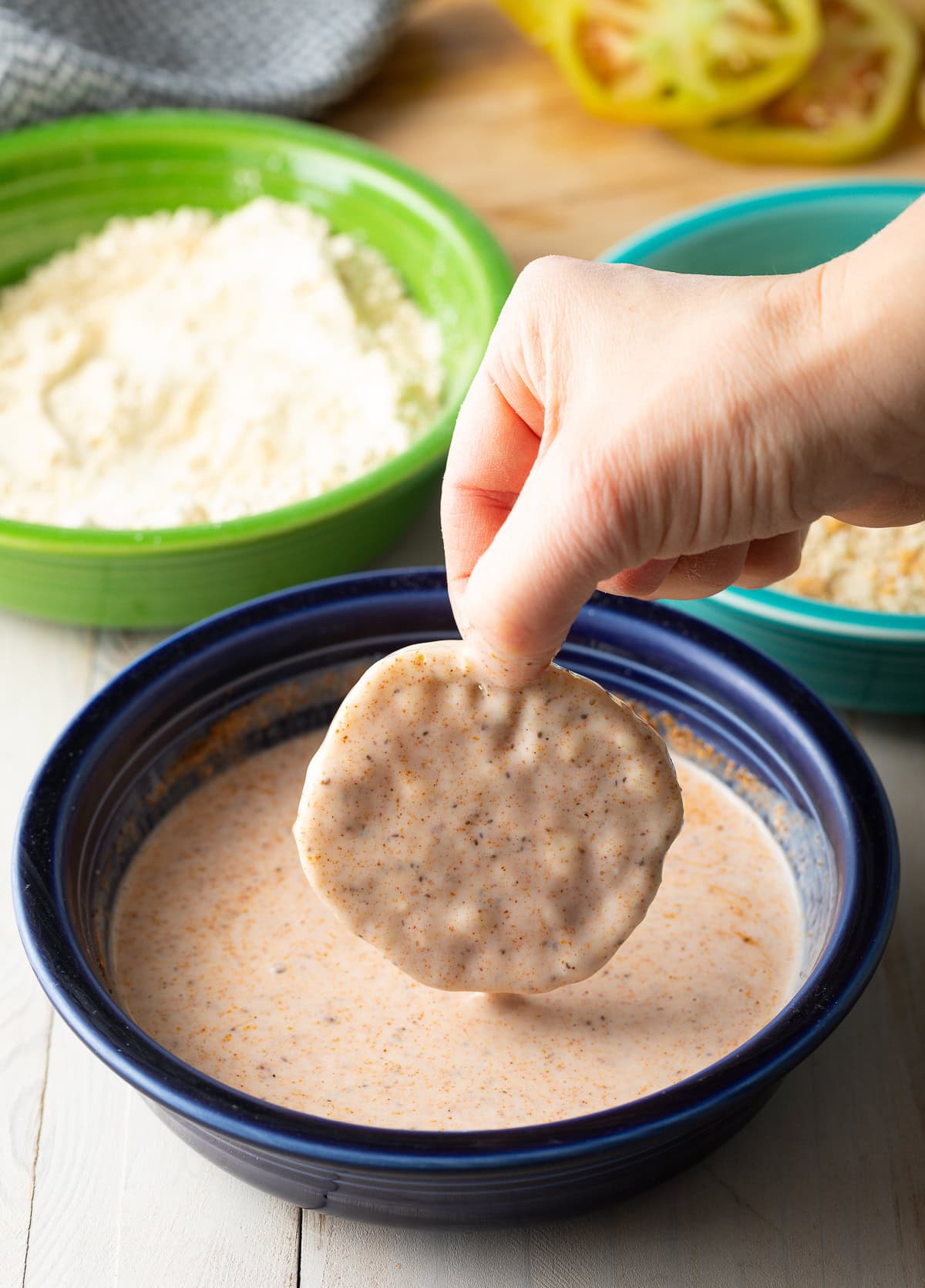 Hand dipping tomato into buttermilk mixture.