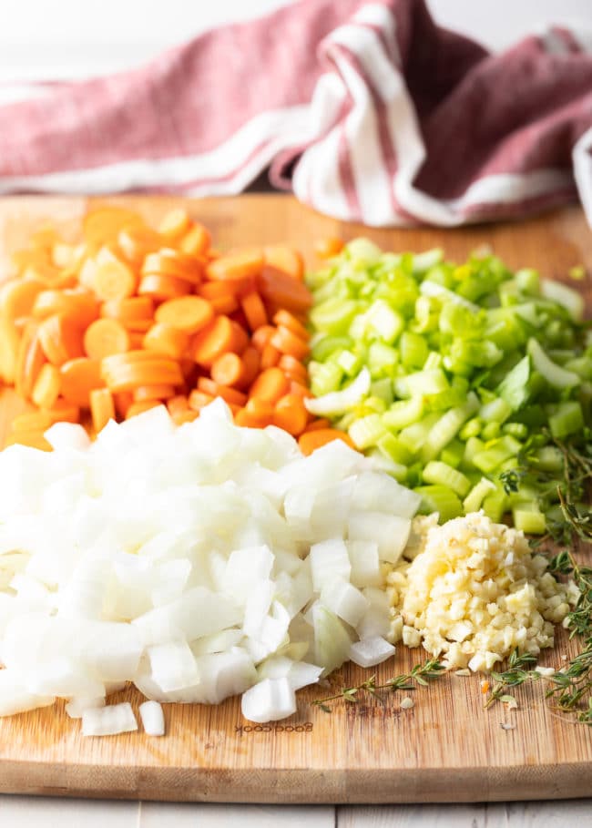 Chopped white onion, carrots, celery and garlic on a cutting board for chicken and rice.