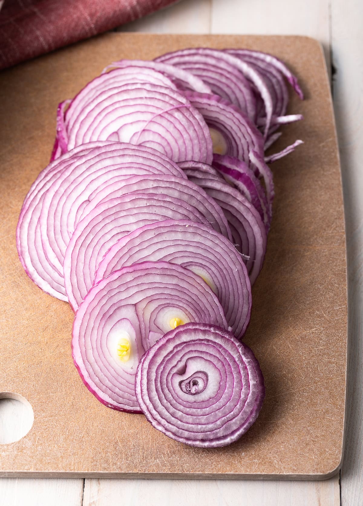 Thinly sliced rounds of red onion on a cutting board.