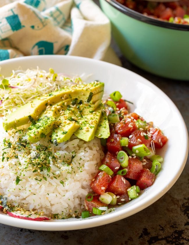 Side view of a loaded up ahi tuna poke bowl topped with fresh avocado and scallions. 