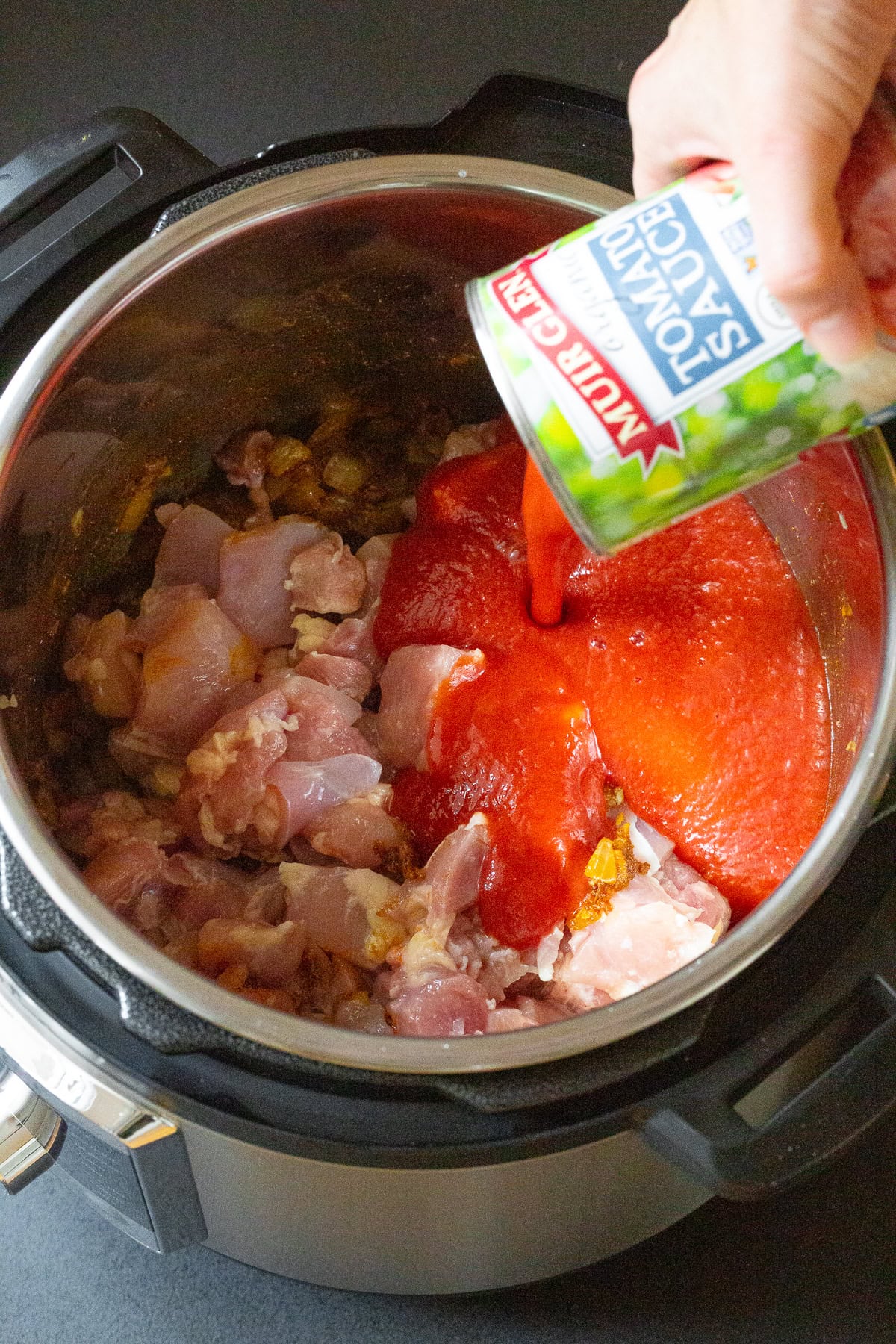 Raw chicken and tomato sauce being poured into instant Pot. 