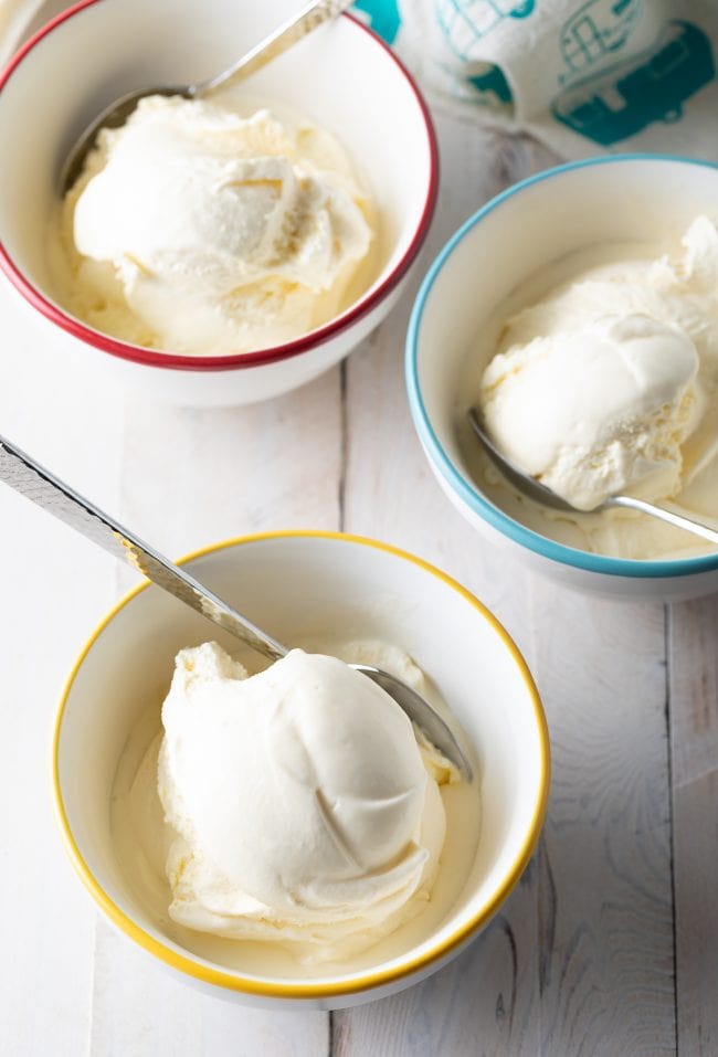Overhead shot of vanilla ice cream scooped into bowls with metallic spoon.