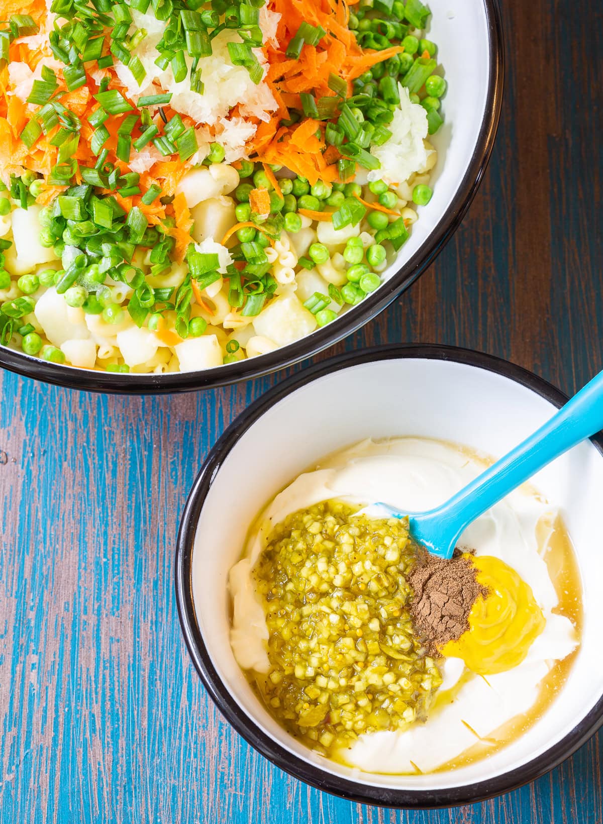 Pasta salad in one bowl with the dressing being mixing in another, smaller bowl. 