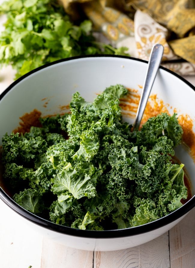 Kale with sauce and spices in a white mixing bowl.