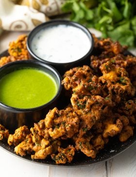 Plate with kale vegetable pakora, with a ramekin of white sauce and ramekin of green sauce.