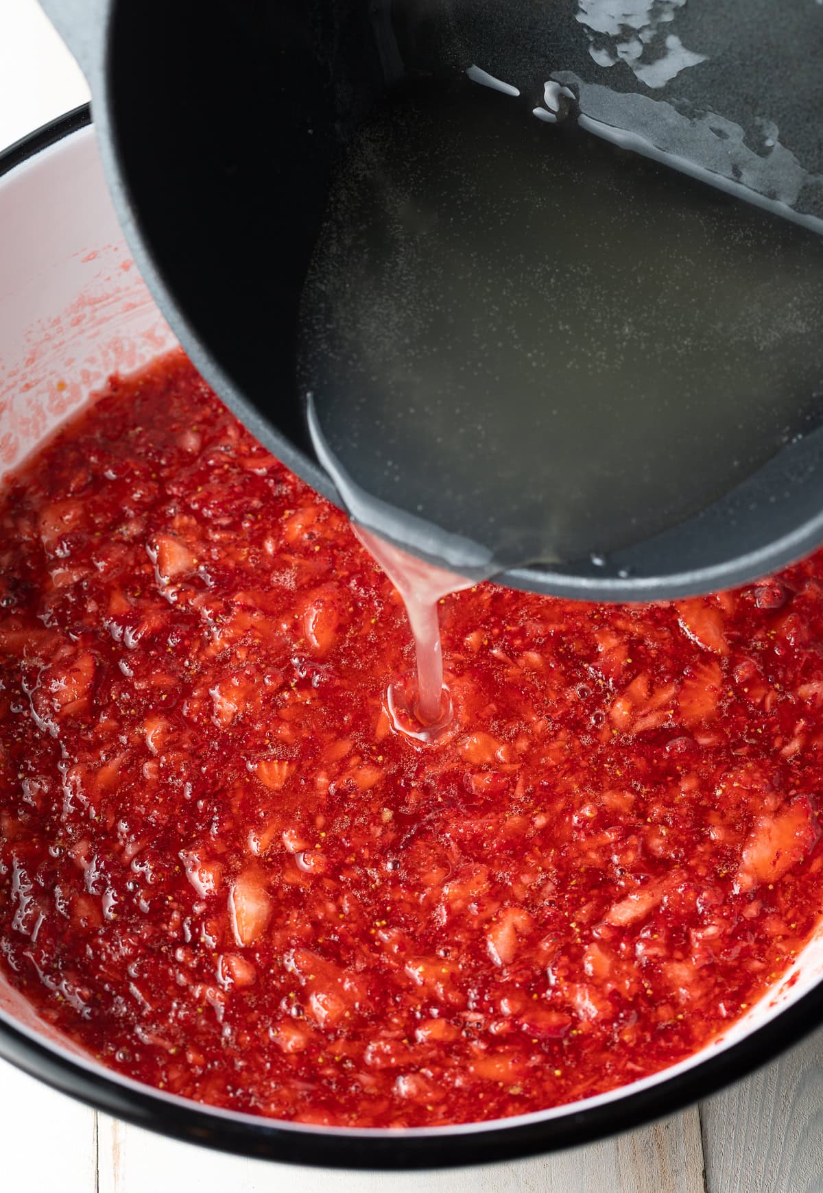 Pectin syrup being poured into fruit mash. 