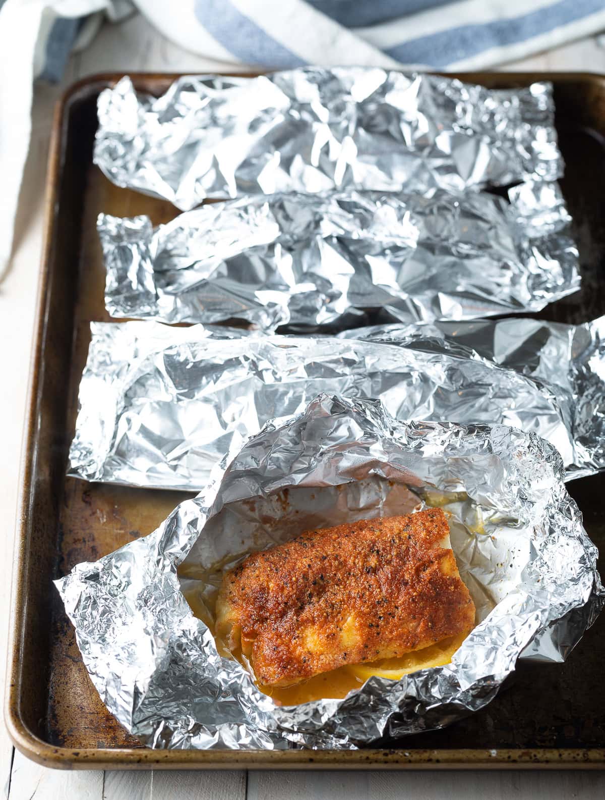 Foil packet pulled open to reveal grilled cod fillet inside. 