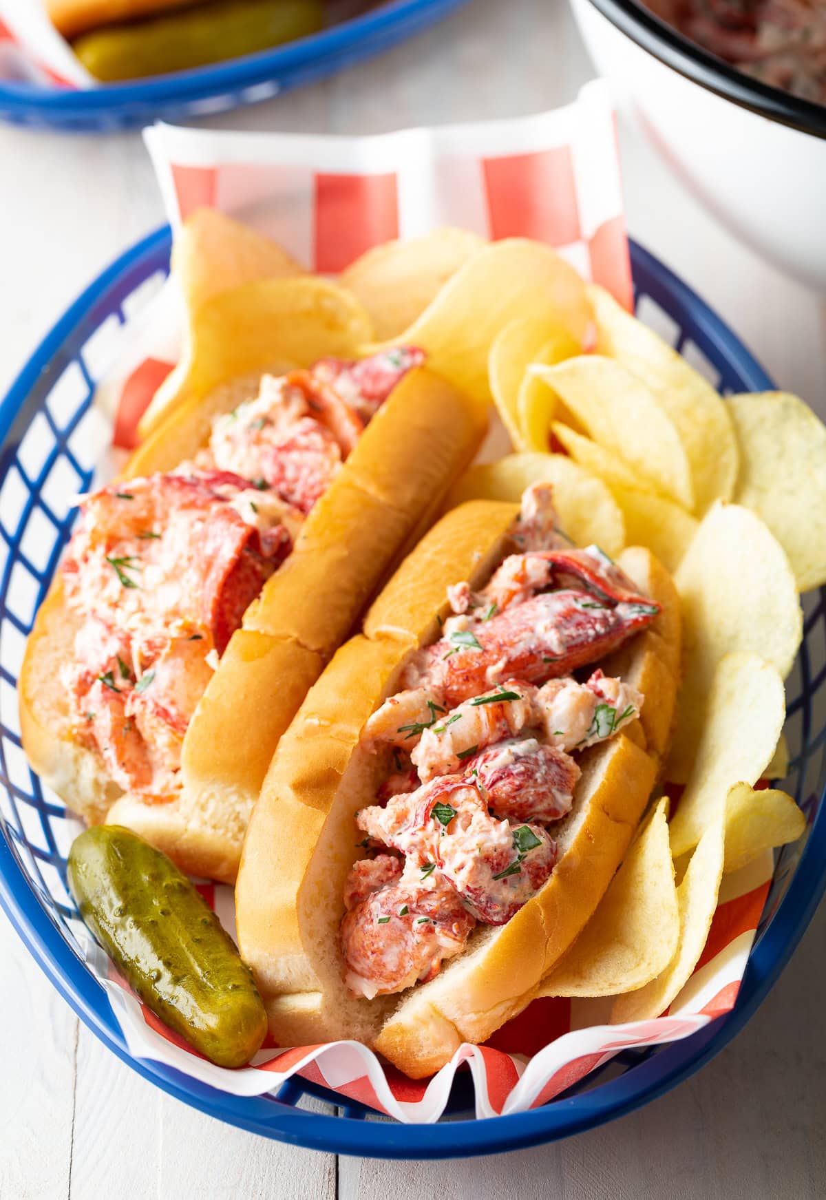 Lobster Roll recipe in a basket with chips and pickle. 