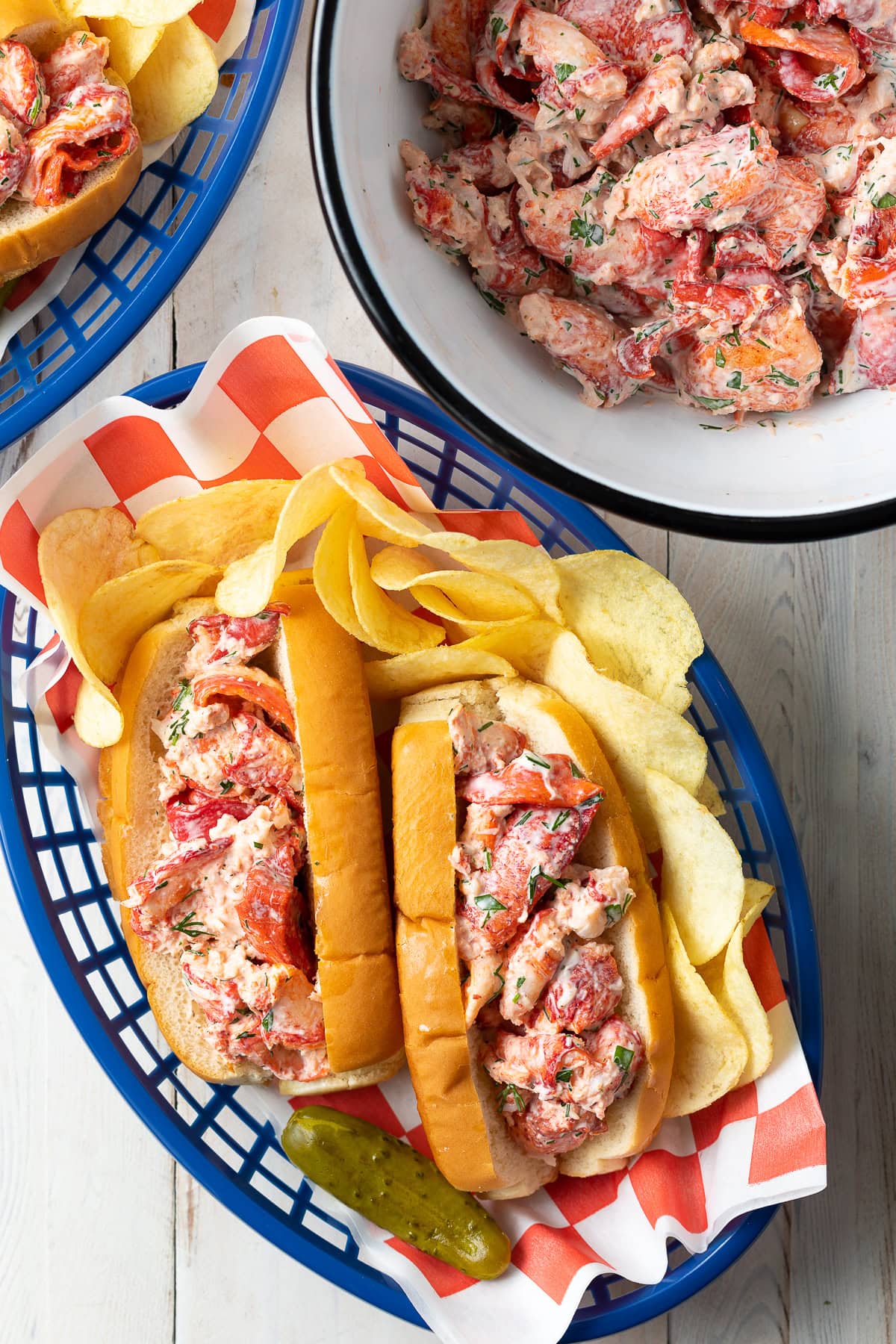 Overhead shot of maine lobster rolls recipe in a serving basket with chips and more lobster in the background. 