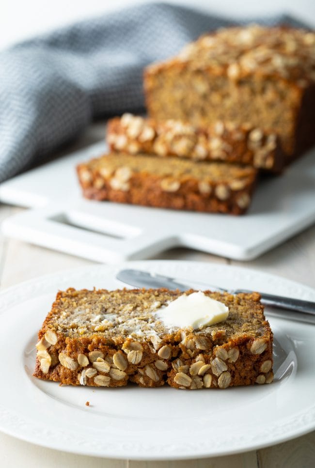 Slice of banana bread on a plate topped off with a smear of butter.