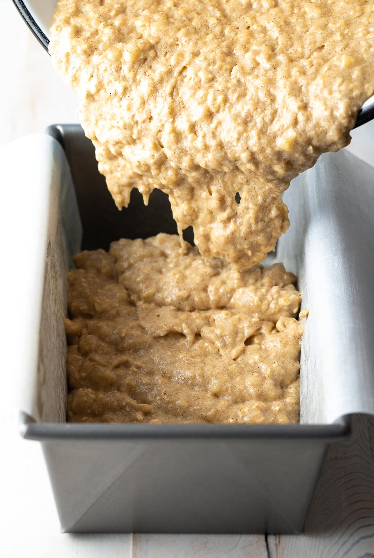 Banana bread batter being poured into a baking dish lined with parchment paper.