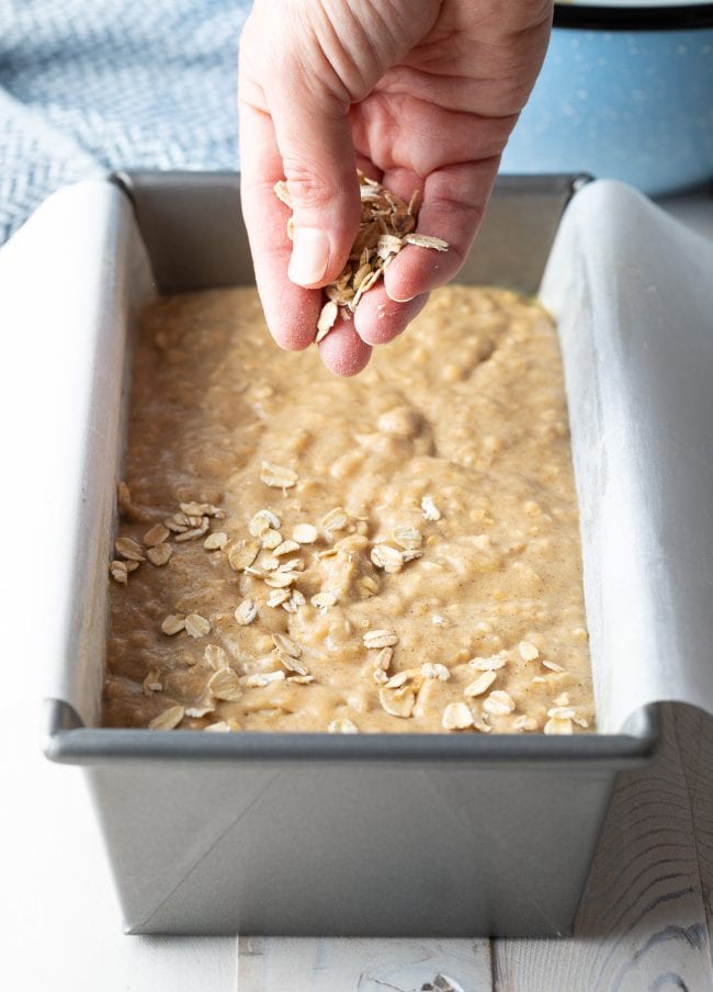 Hand sprinkling oats onto banana bread batter.