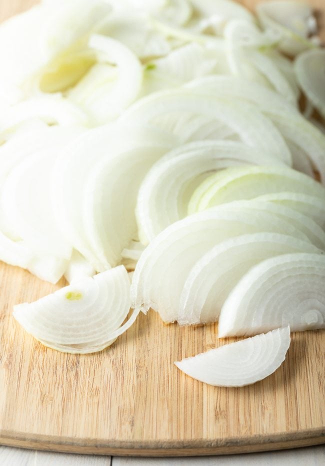 Wooden cutting board with sliced onion halves.