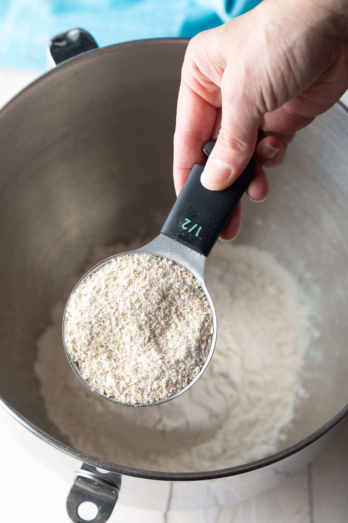 Hand with a measuring scoop adding oat flour to a metal mixing bowl.