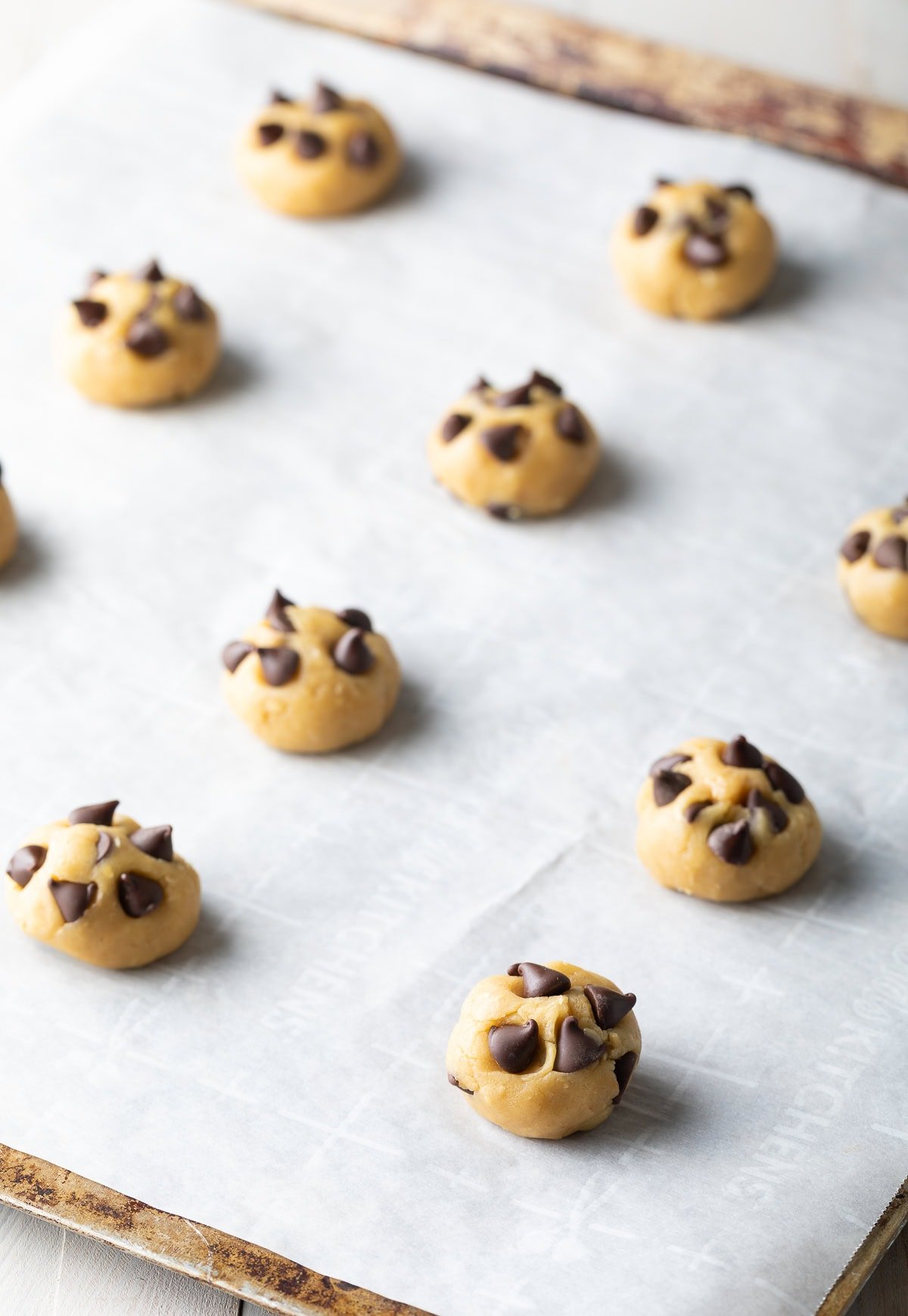 A dozen raw chocolate chip cookie dough balls on a baking sheet.