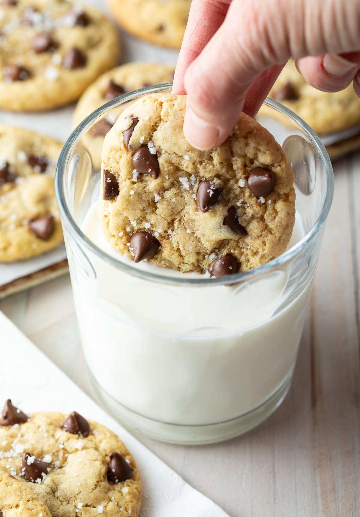Hand dunking a chocolate chip cookie into a glass of milk.