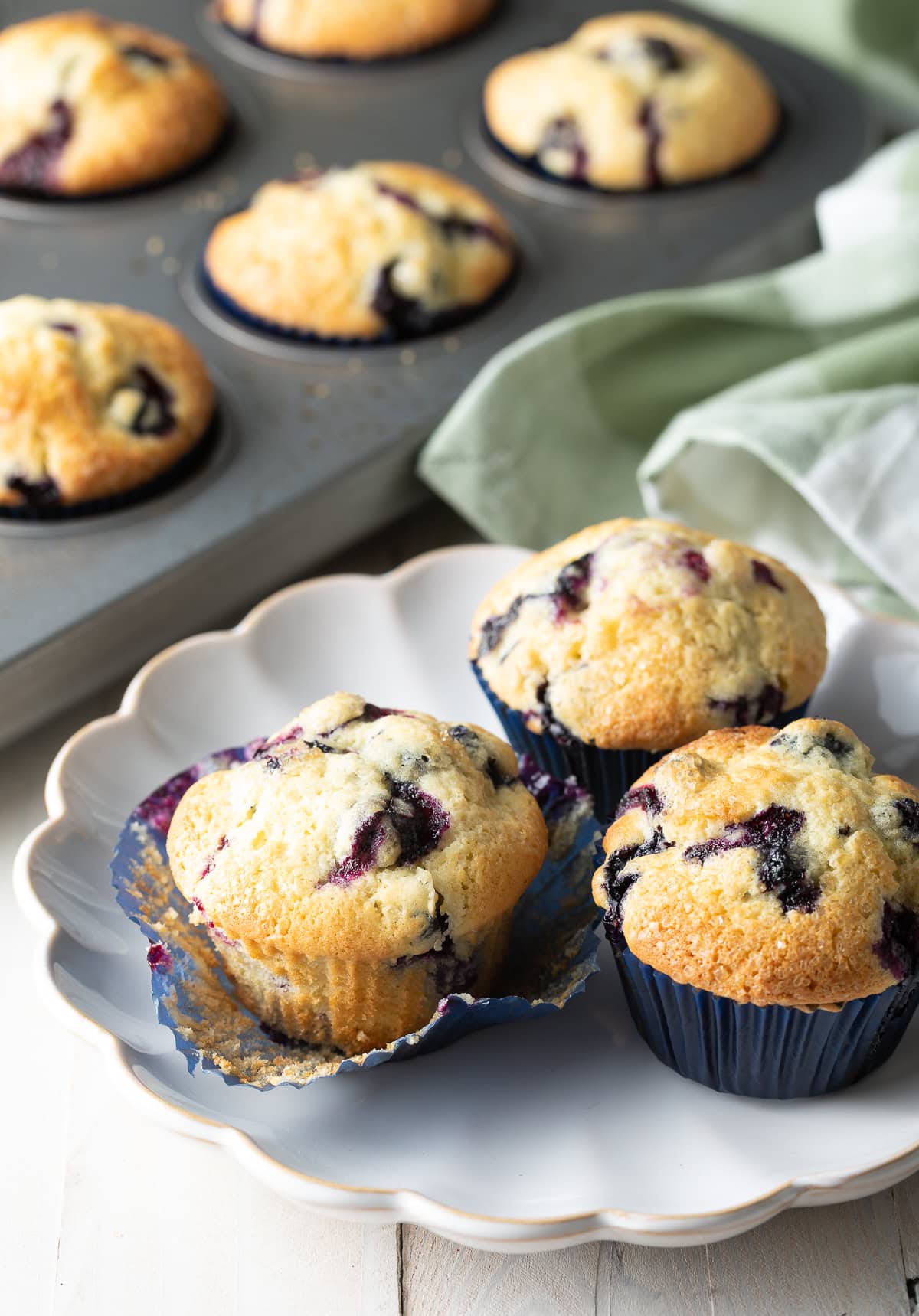 A plate of three blueberry muffins made from a homemade blueberry muffins recipe.