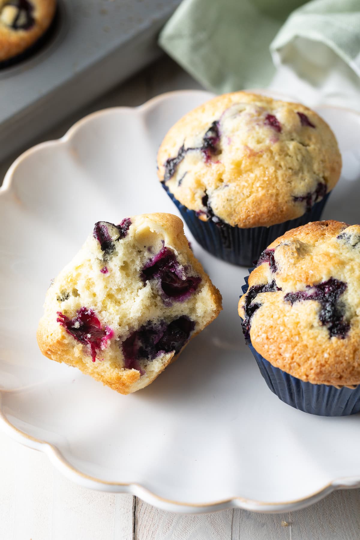 Three blueberry muffins on a white plate, one cut in half.