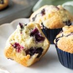 Three blueberry muffins on a white plate, one cut in half.