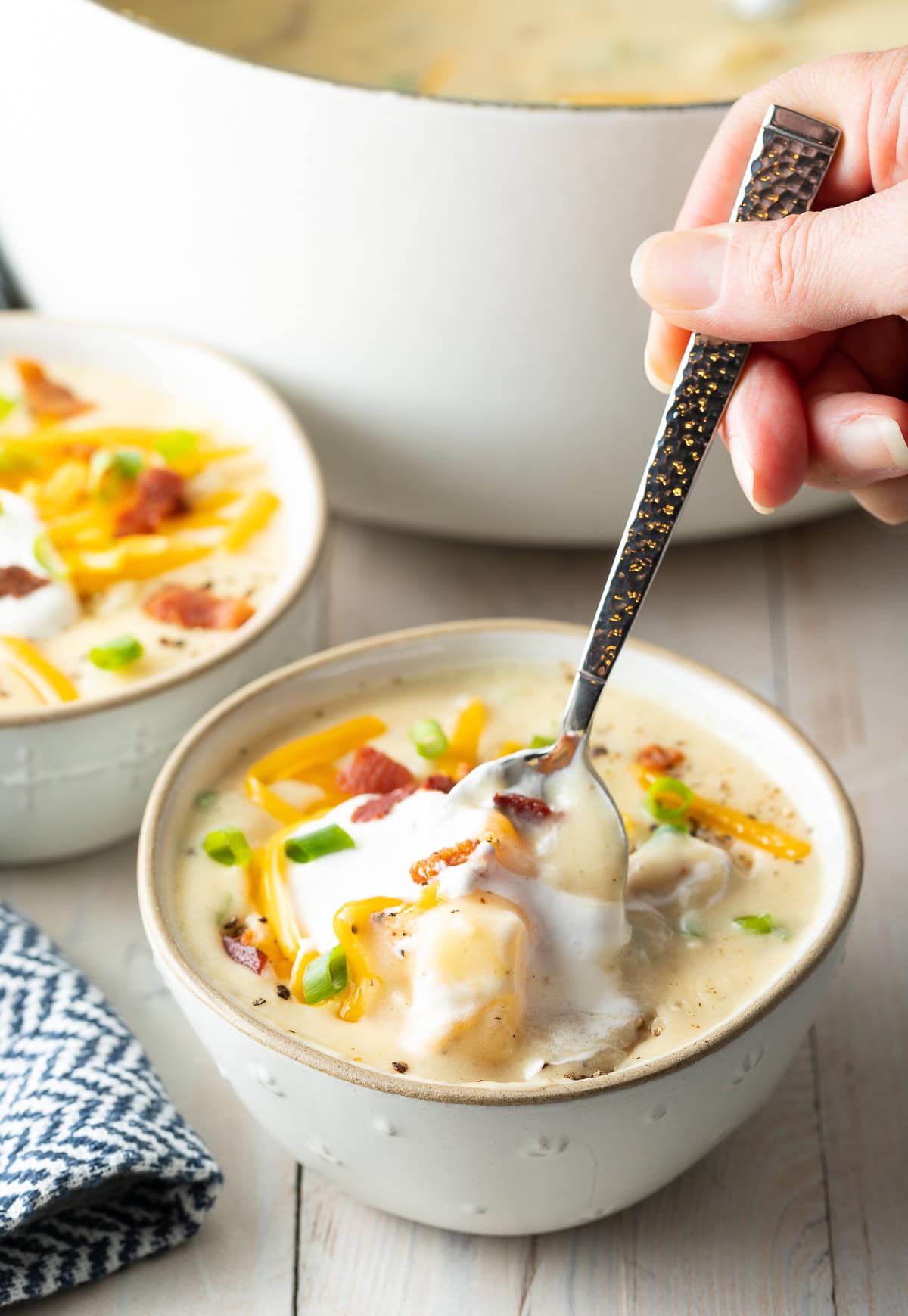 Hand holding a spoon that is going into a bowl of creamy potato soup.