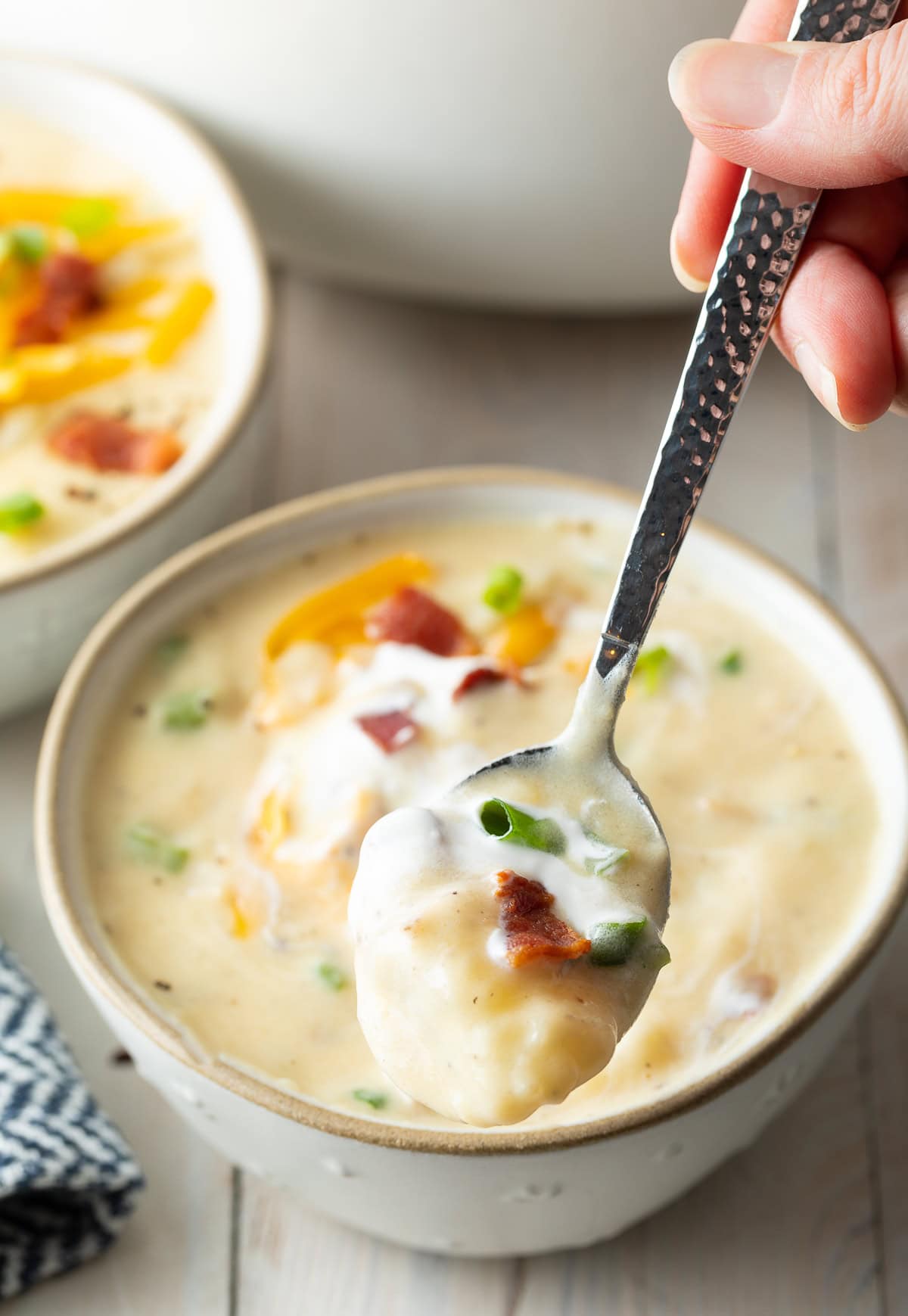 Bowl of chunky potato soup with a hand holding a spoon with a scoop.
