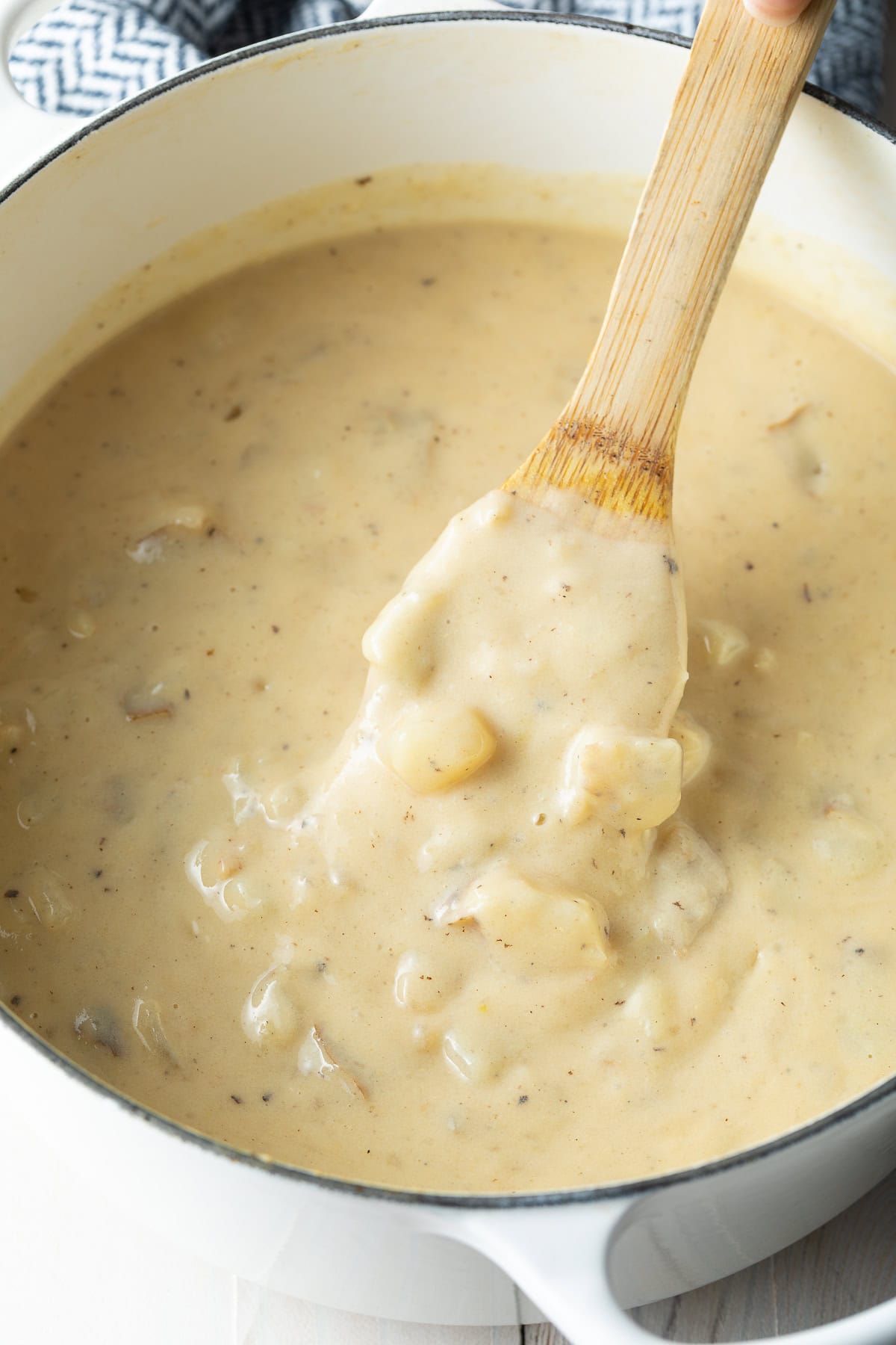 Creamy potato soup in a white pot with a wooden spoon.