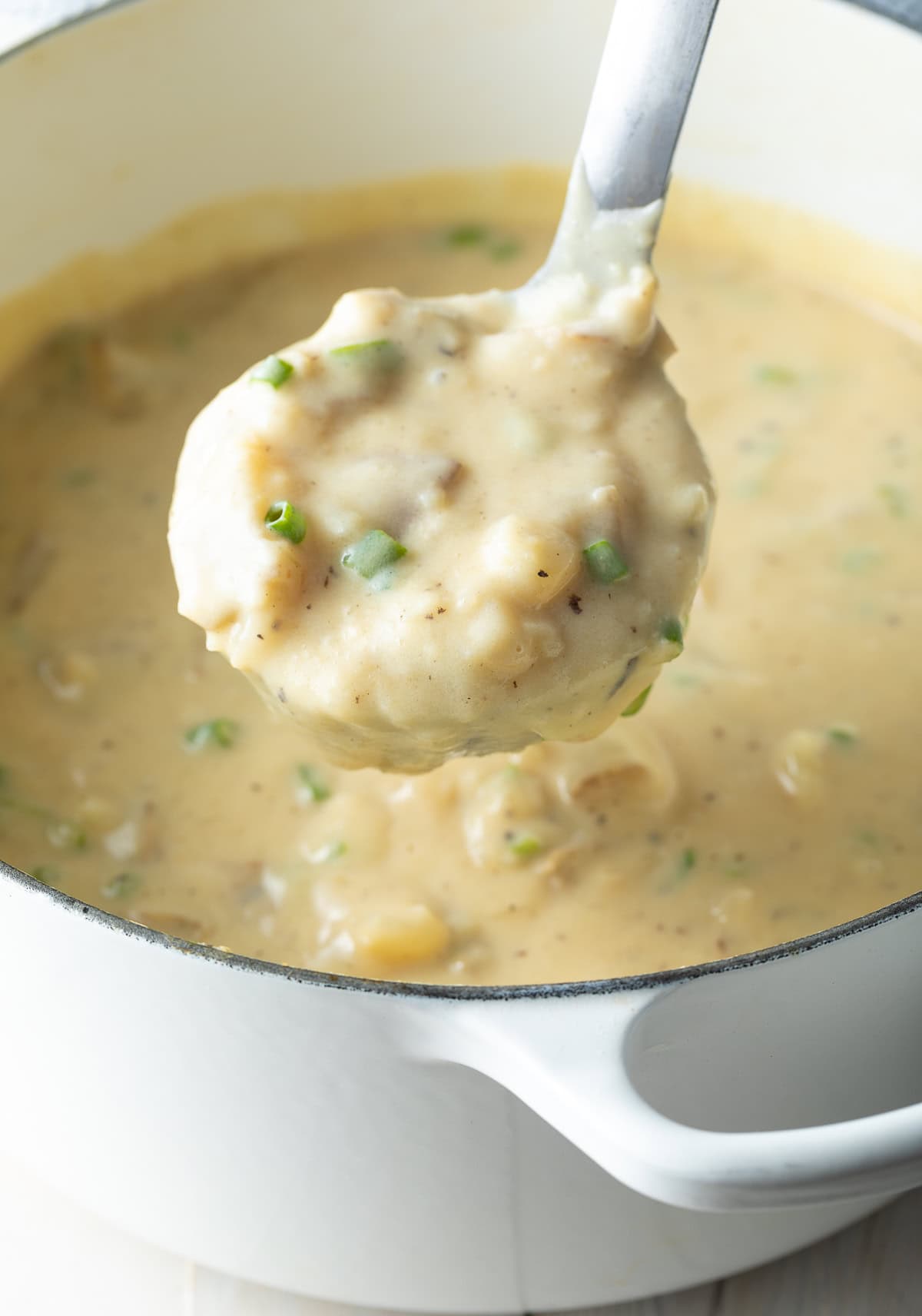 Loaded potato soup in a white pot with a ladle taking out a scoop.