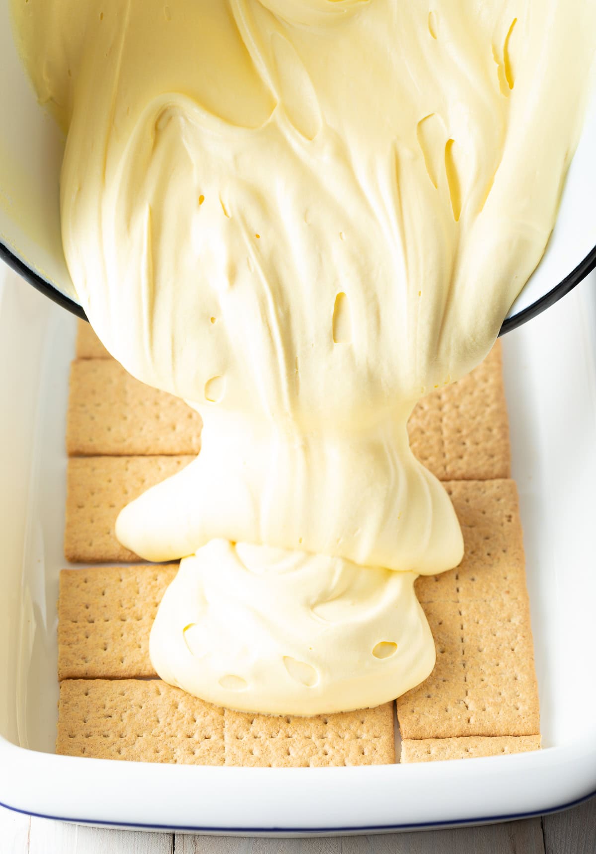 Baking tray lined with a single layer of graham crackers and the creamy layer being poured on top.