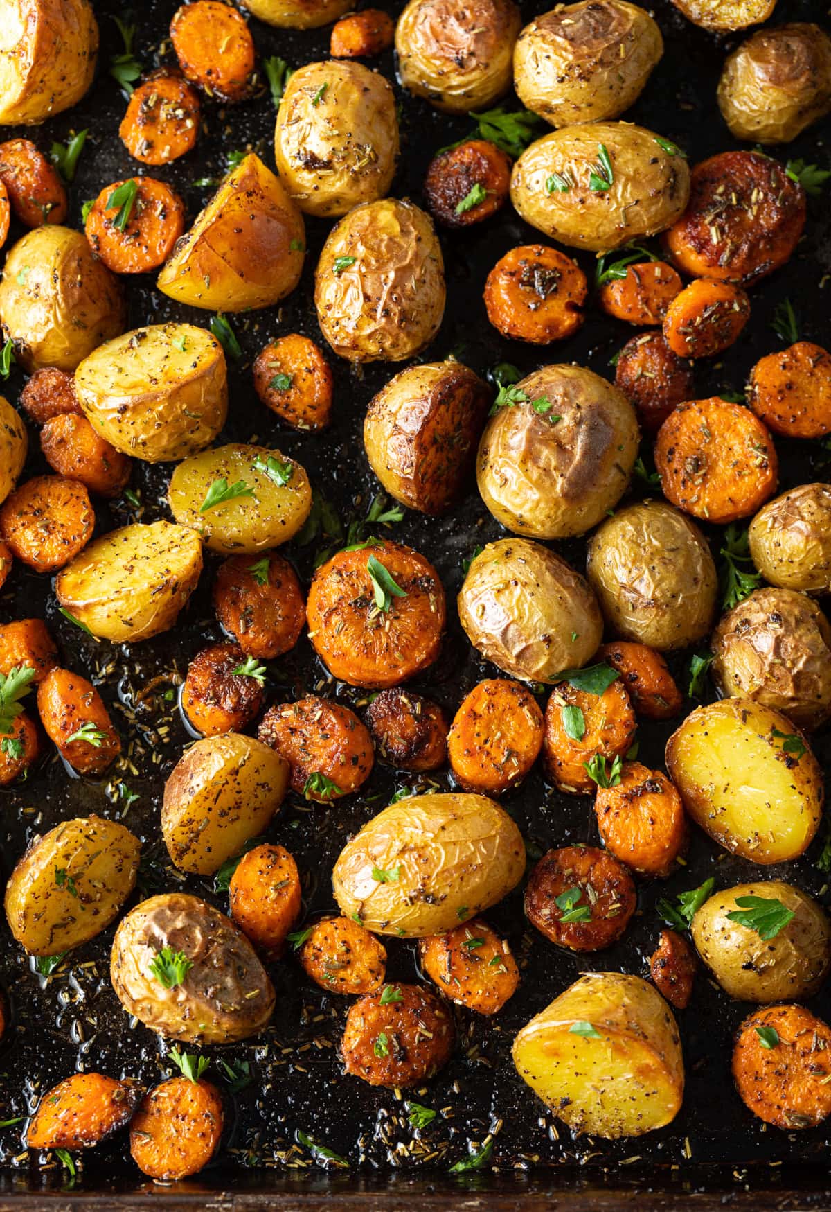 overhead of roasted carrots with potatoes and fresh herbs on a baking sheet
