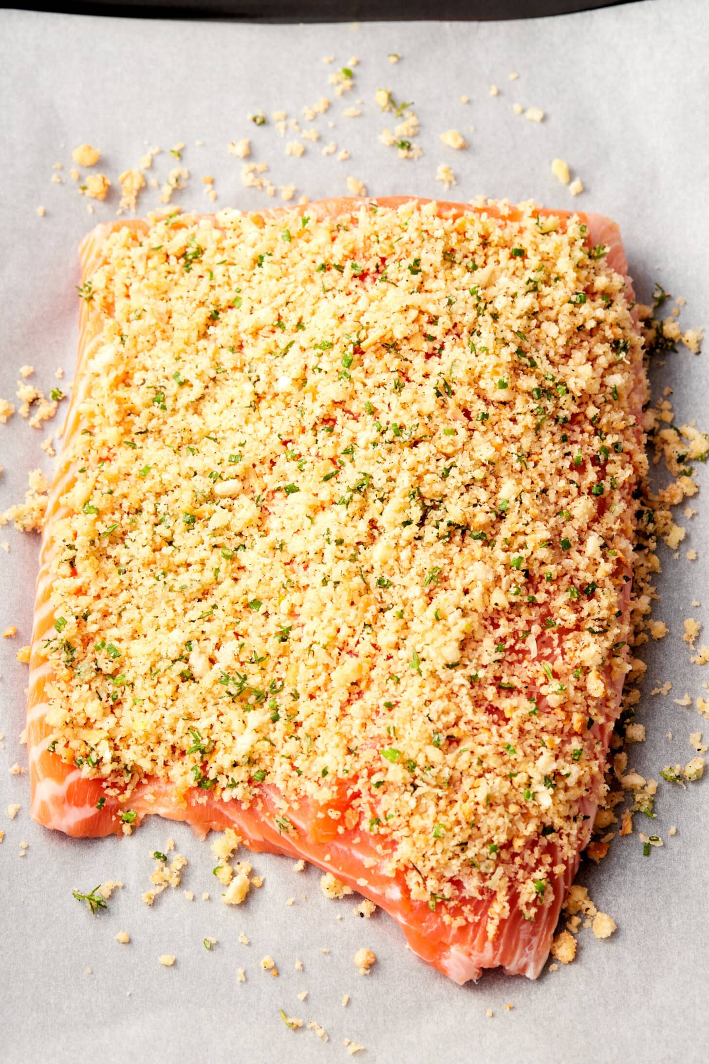 Salmon with parmesan crust on parchment paper before being baked.