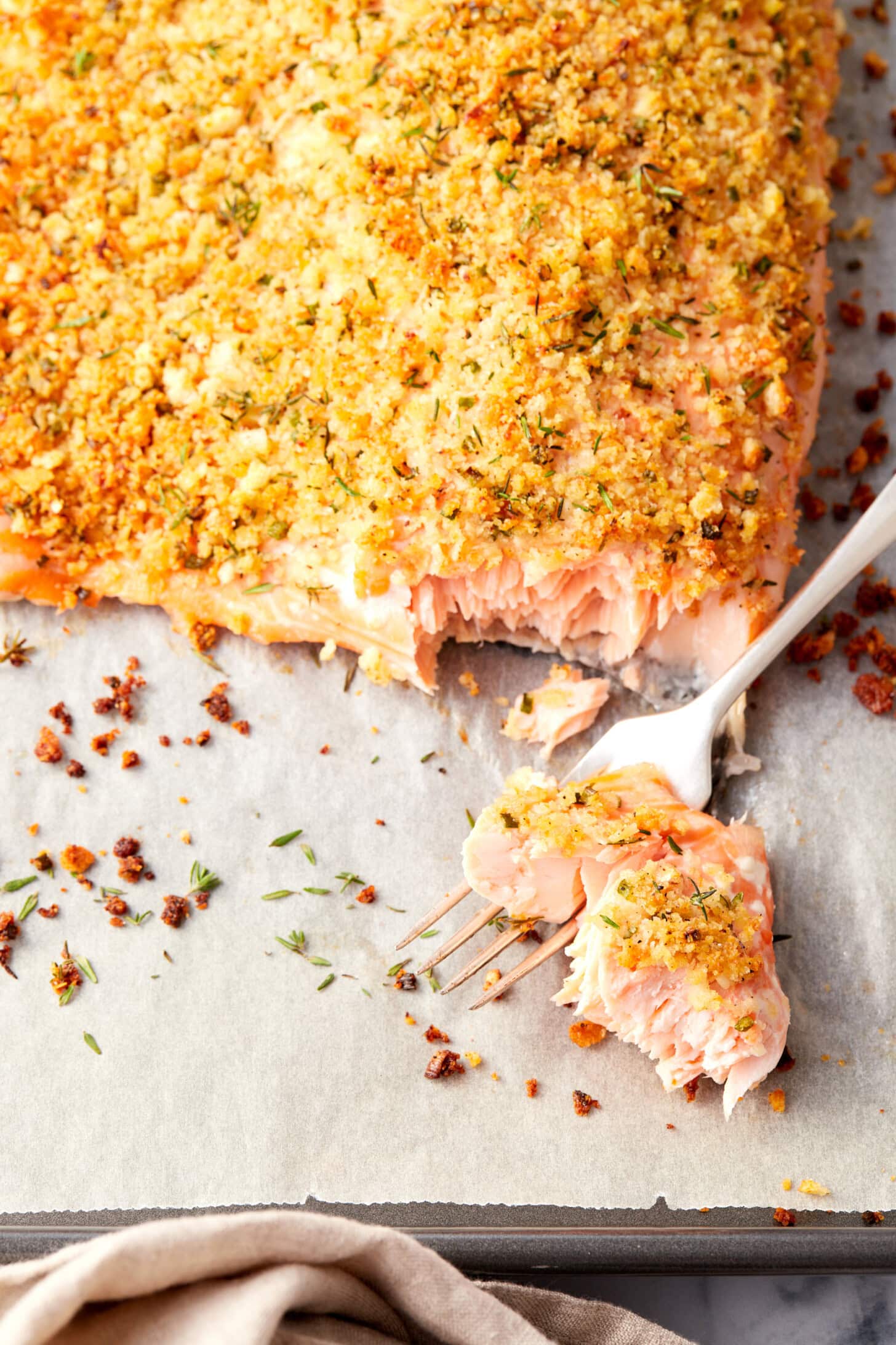 Fork removing piece of cooked flaky parmesan crusted salmon. 
