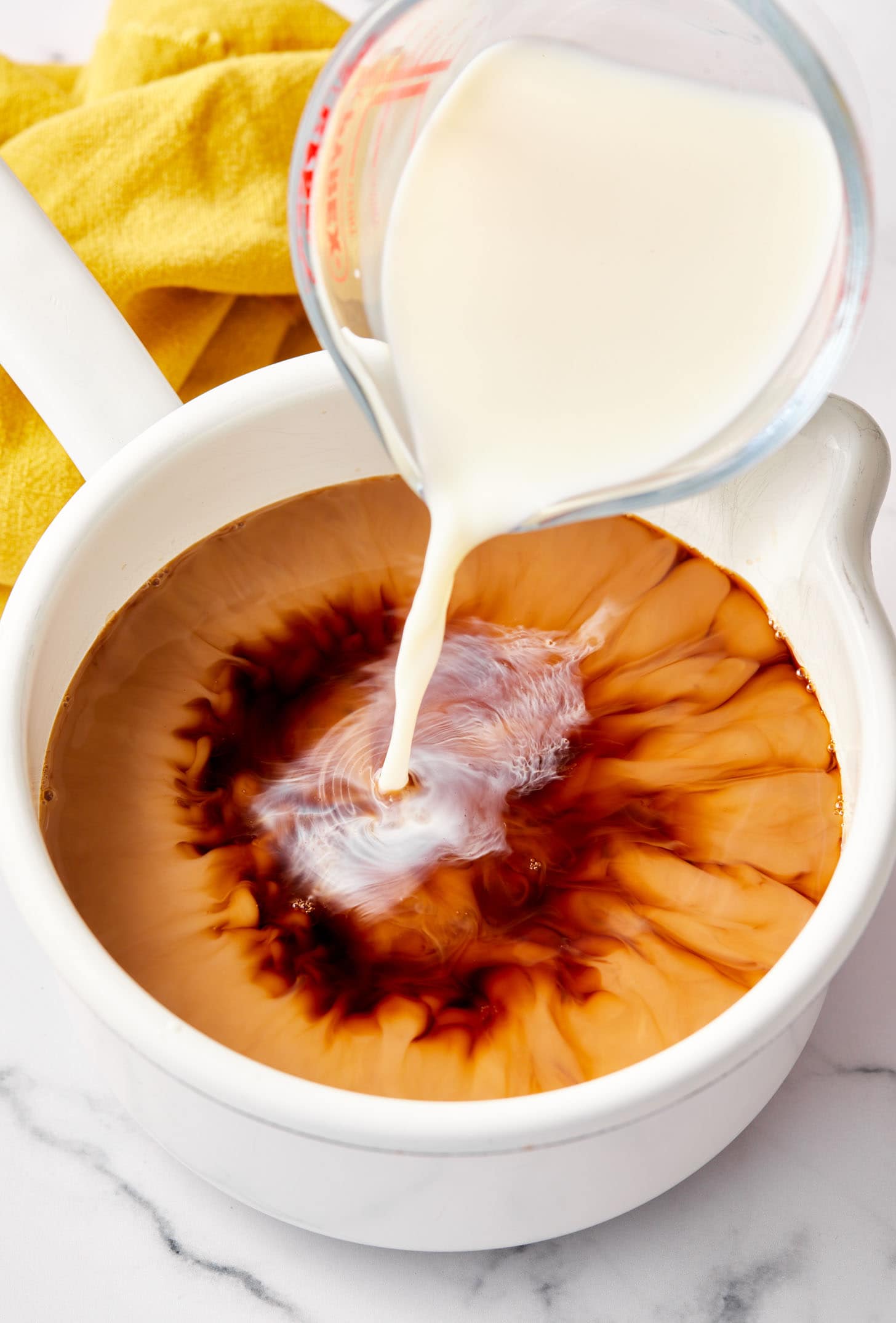 Milk being poured into a pot of chai tea recipe.