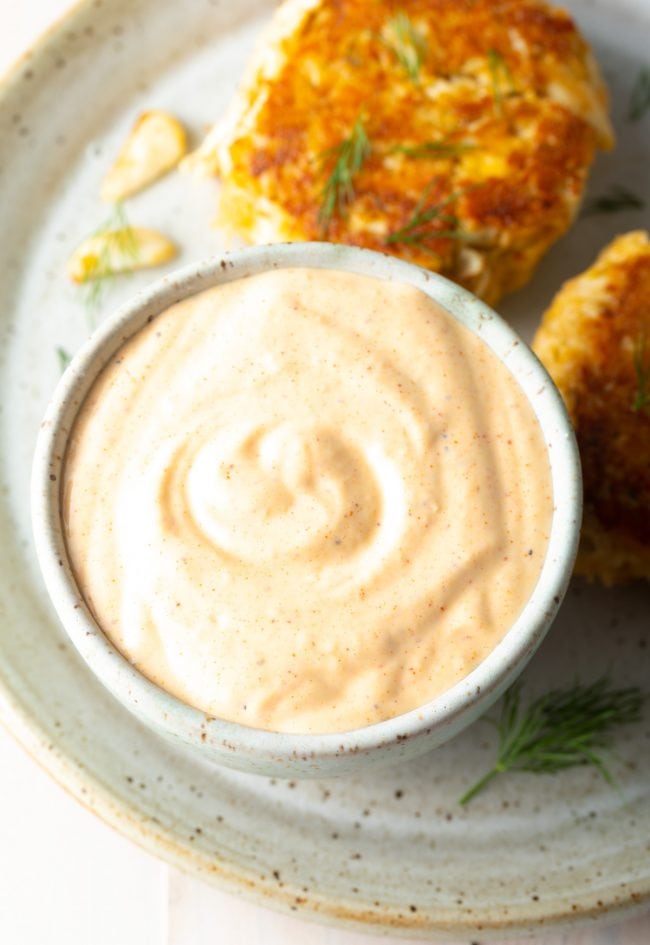 Top down view of a plate of crab cakes served with a small ramekin filled with remoulade sauce.