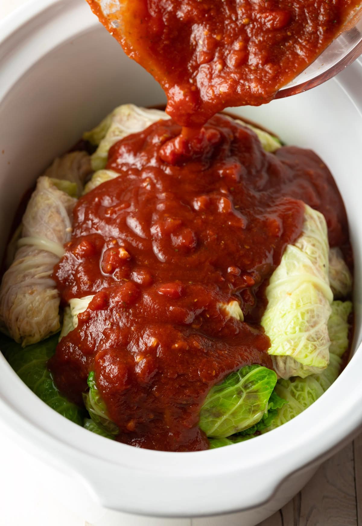 Close up of cabbage rolls in slow cooker with sauce being poured on top.