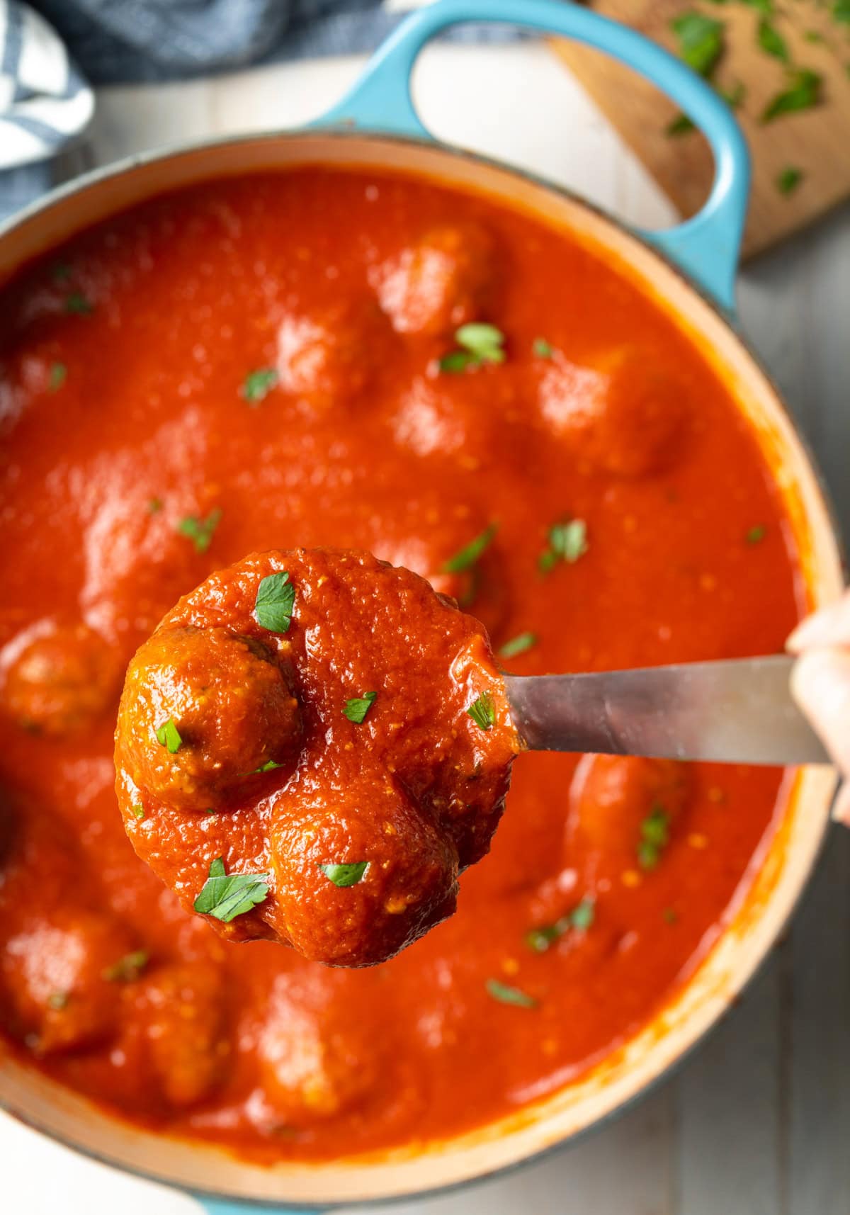 Ladle lifting tomato sauce and baked meatballs up out of pot